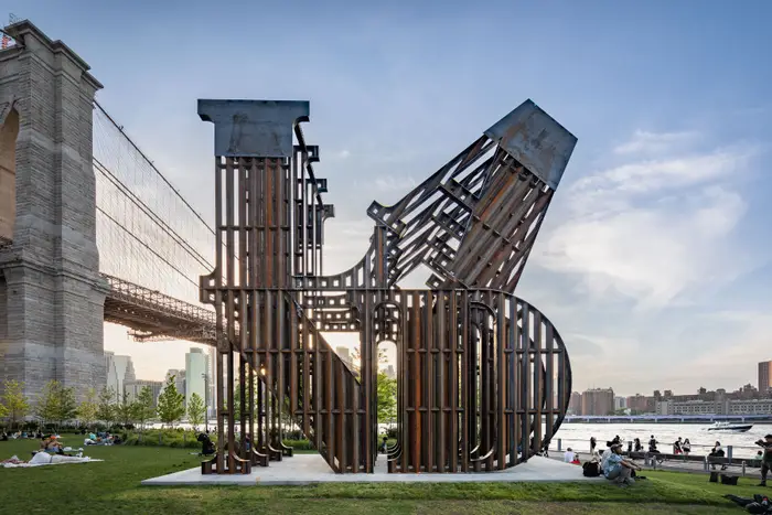 A huge sculpture that spells the word "LAND" in oversize letters, in front of a bridge in a park
